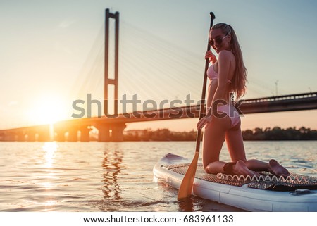 Woman on stand up paddle board. Having fun on SUP board during sunset. Active lifestyle.