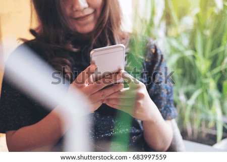 A beautiful Asian woman using and looking at smart phone in modern cafe with green nature background
