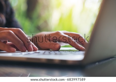 Closeup image of a business woman's hands working and typing on laptop keyboard on glass table with green nature background
