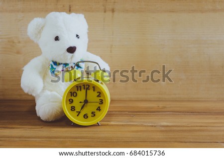 Teddy Bear and alarm clock on wood background.