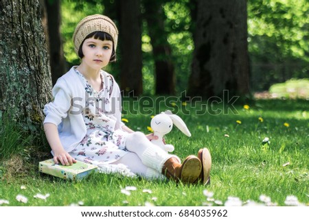 Little cute girl reading a book under big linden tree