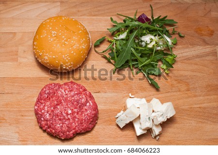 Picture of a cheeseburger before frying, meat, burger bun, gorgonzola cheese and rucola