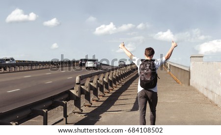 Stylish young man with a backpack walking on a bridge