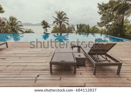 A long chair next to the pool with clear water and mountain and forest views in front. A place to rest. This image has a retro feel because it uses film tones.