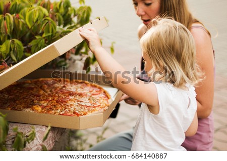 Mom and daughter open a box of pizza.