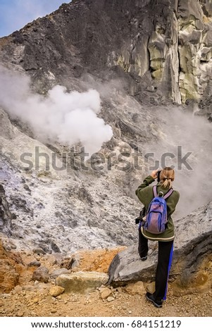 Female trekker and photographer taking images of evaporating sulphur from the crater of the Gunung Sibayak volcano in Sumatra, Indonesia