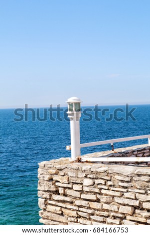 Rock wall with white lantern at the edge with blue sea in the background. Travel, swimming, natural landscape, summertime, Mediterranean, Adriatic sea.