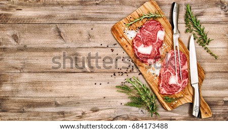 Raw meat ribeye steak with herbs and spices on wooden kitchen desk. Food background. Rib eye. Vintage style toned picture