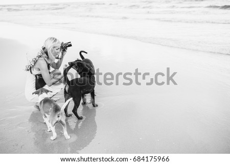 Young female blonde woman shooting on the beach and plays with dogs. 