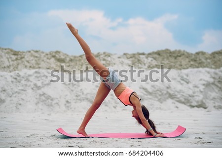 Sporty yoga girl on the beach practices backward kicks leaning on her hands. Sport and healthy lifestyle concept.