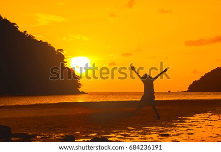 Silhouette of happy girl jumping on the beach, sunset background.