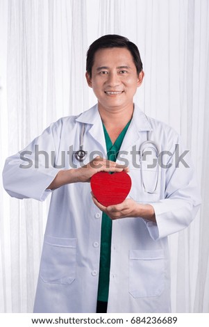 Asian male doctor with stethoscope holding heart, isolated on white background