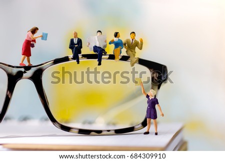 Miniature people reading and sitting on book with glasses using as background, education or business concept.
