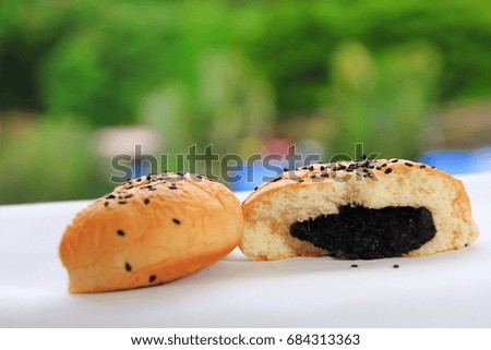 The soft bun filled with the combination of black sesame black bean and sugar placed on the white table surface and on the real scene of the green forest background in the sunny day time 