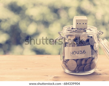 Saving money for house,coins in glass jar with quote house on wood table with pastel blurred background