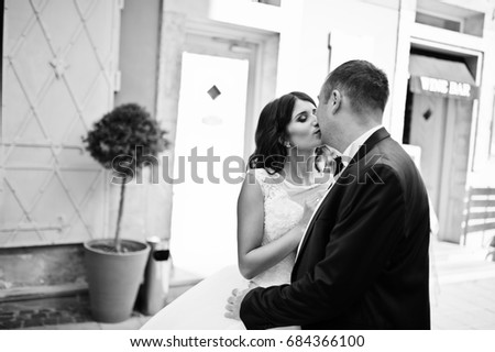 Stunning young wedding couple kissing on the street of the old town with great architecture. Black and white photo.