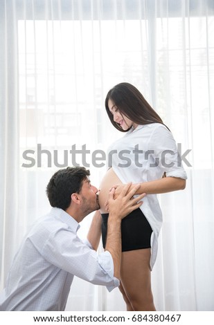 Happy Family with Asian Husband Kiss on the Belly of His Wife Meaning to Take Care with Love in the Room - Family Concept