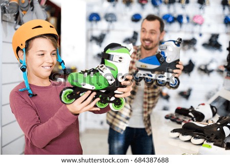 positive germany male shop assistant helping boy to choose roller-skates in sports store
