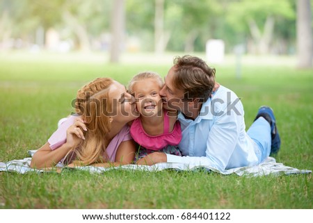 Father and mother kissing their daughter on both cheeks