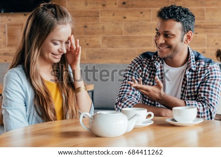 Smiling young man talking to shy woman sitting in cafe Royalty-Free Stock Photo #684411262