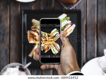 Taking food photo, food photography by smart phone, club sandwich with french fries on wooden table