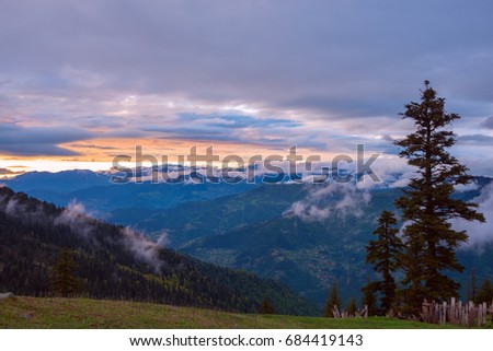 Amazing sunset in a mountains after storm - golden strip on the horizon and colorful purple clouds floating over mountain ranges, in the rays of setting sun.