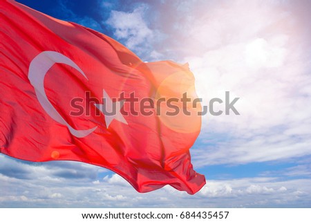 Turkish flag against a blue cloudy sky. Flag of Turkey in sunlight and glare. Red flag with a crescent and a star. Royalty-Free Stock Photo #684435457