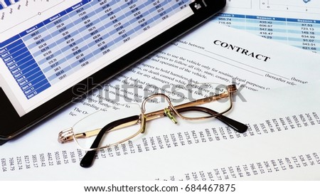 Glasses lies on the table. Contract document and other papers with business information are under it.