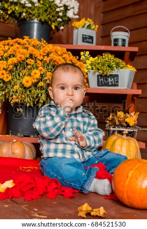Cute, handsome boy with bright emotion smiling sitting near pumpkin and hay on the floor with autumn flowers