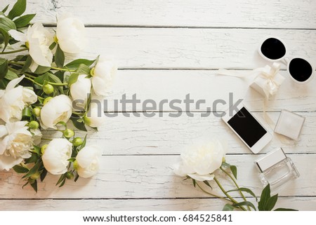 Bouquet of white peonies, phone and a bottle of perfume on the wooden table, soft focus background