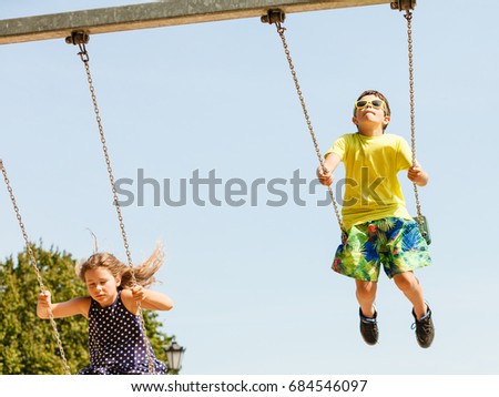 Fun and joy of children. Little girl and boy playing outdoor on preschool playground garden. Kids swinging on swing-set to touch the sky. Royalty-Free Stock Photo #684546097