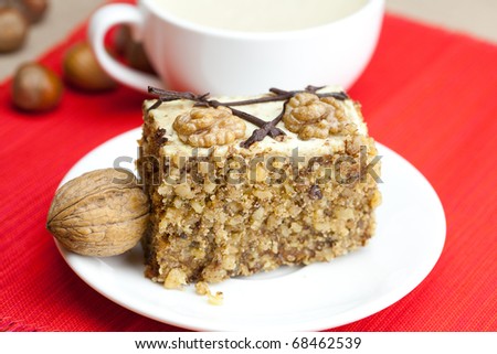 cup of cappuccino, a piece of cake with nuts on a plate lying on a red background
