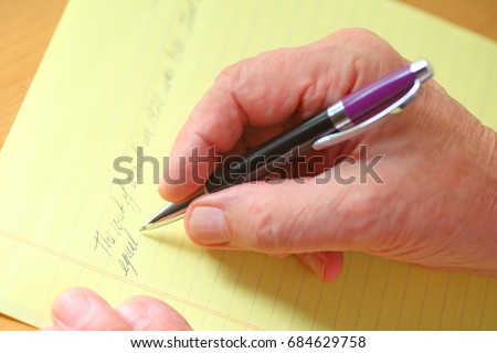 Older man writes in cursive on a ruled yellow pad of paper Royalty-Free Stock Photo #684629758