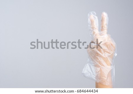 Hand wearing disposable protective plastic glove with victory gesture on white background
