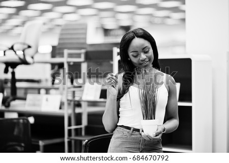 Stunning african american woman holding lovely small plant in the store. Black and white photo.