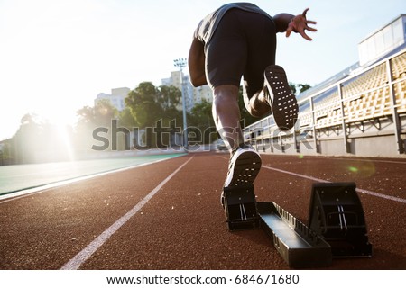 Back view of a young male athlete launching off the start line in a race Royalty-Free Stock Photo #684671680