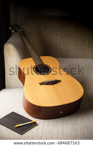 The acoustic guitar and notebook on the sofa with soft sunshine through in dark room. vignette picture tone