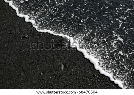 diagonally divides picture containing black lava sand and smooth ocean water with a pebble in the middle