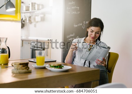 Morning routine. Woman reading newspaper during breakfast at her home Royalty-Free Stock Photo #684706051