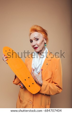 Picture of gorgeous mature redhead fashion woman standing isolated at studio holding skateboard. Looking at camera.