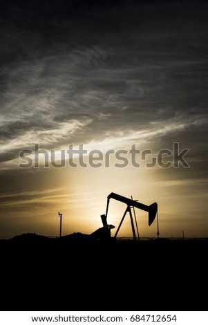 Silhouette of crude oil pump in oilfield with cloudy sunset background.
