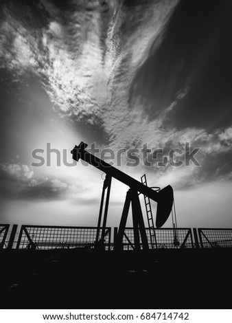 Silhouette of crude oil pump in oilfield with cloudy sunset background - black and white edit