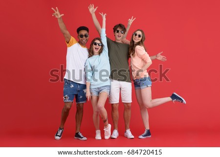 Picture of young happy group of friends standing isolated over red background. Looking at camera.