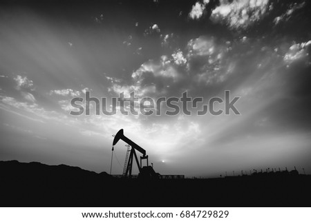 Silhouette of crude oil pump in oilfield at cloudy sunset - Black and white edit 