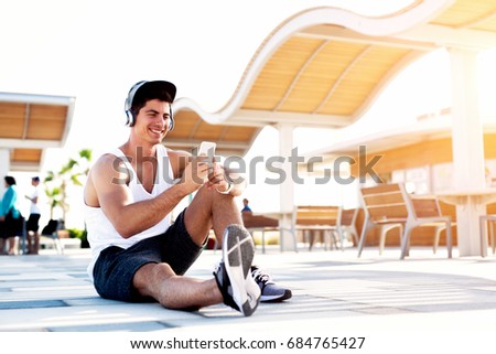 Portrait of young man sitting on ground listening to music on smart phone.