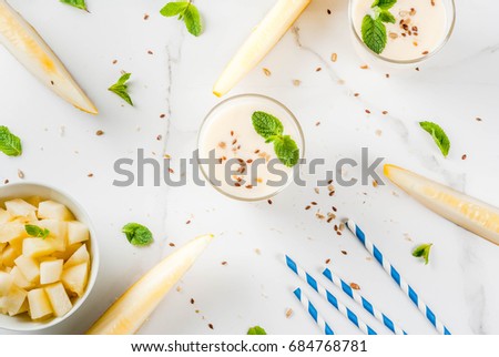 Summer fruits, refreshing drinks. Vegan food. Breakfast. Smoothie of yogurt, raw organic yellow melon, flax seeds and mint. With striped straws, in glasses, white marble table, copy space  top view