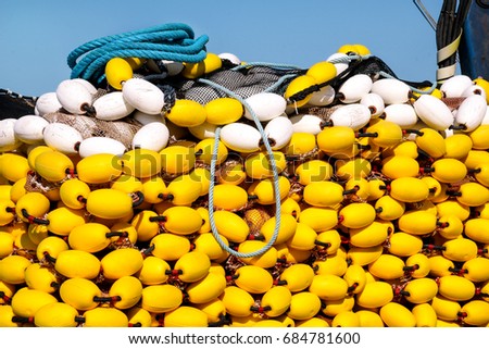 Yellow floats on the pile, covering fishing nets on the blue boat in the summer sun, close up. Fishing floats with rope knot netting piled in a fishing boat.