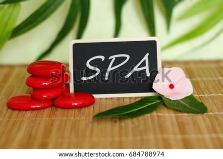A slate with a spa message next to red pebbles arranged in zen lifestyle on bamboo wood floor with a peony flower