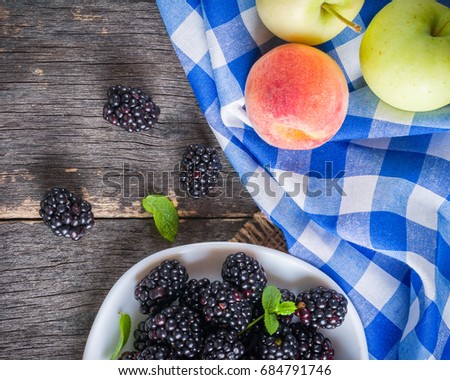 A bunch of blackberries on a white saucer. Gray wooden background. Blue checkered napkin.