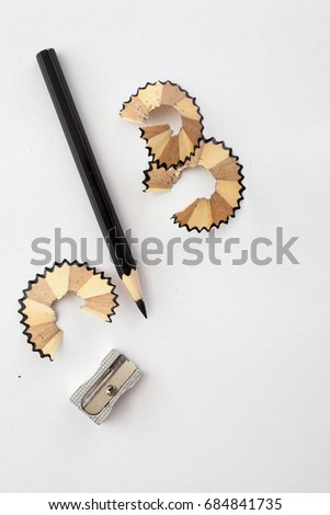 black wooden pencil, sharpener and pencil shavings on white paper
